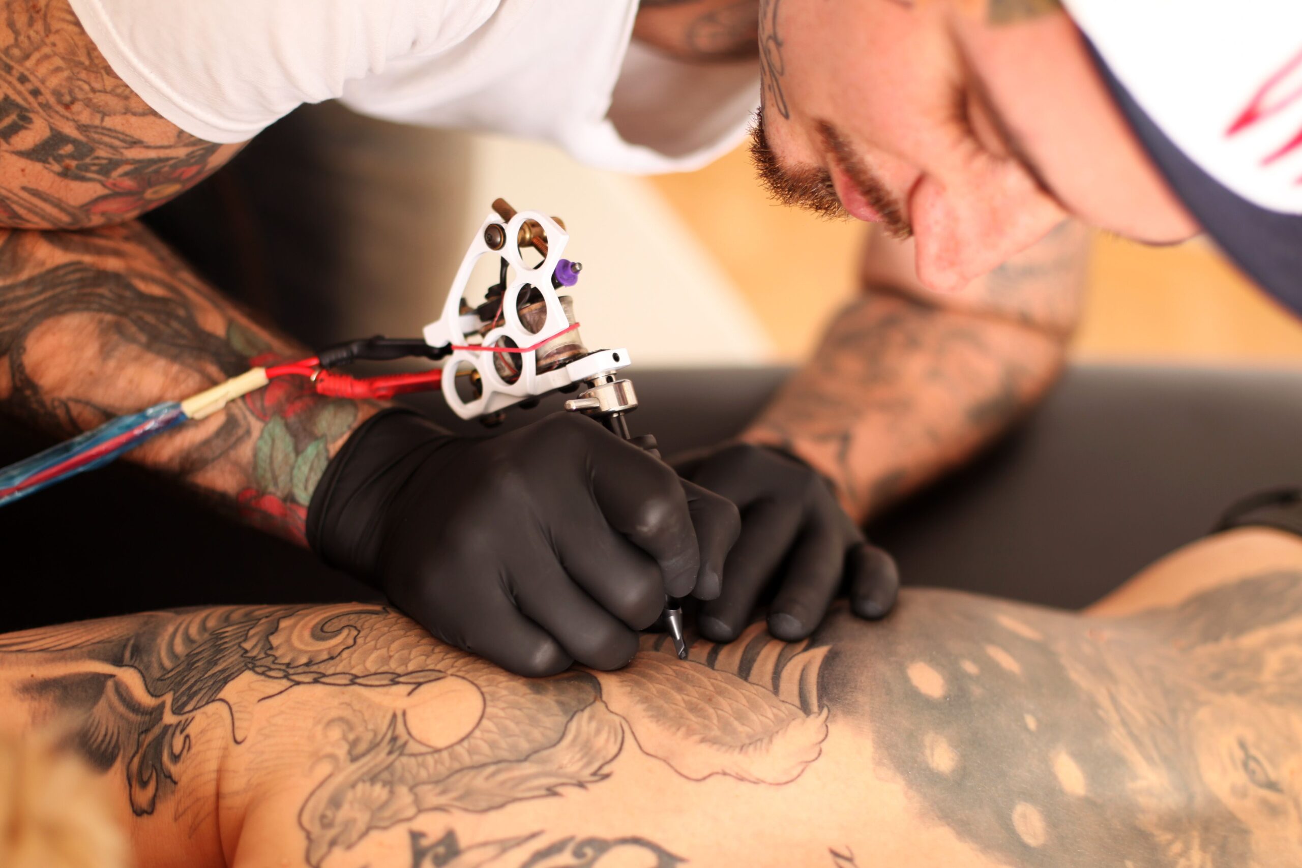 Tattoo artist focusing intently on tattooing intricate designs on a client's back, showcasing elaborate artwork and professional technique.